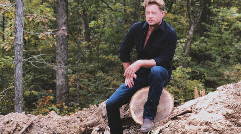 Brandon sitting on a recently-felled tree trunk, with forest in the background..