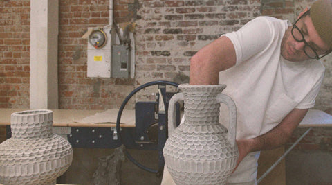 Brian in his studio with his hand inside a ceramic vase.