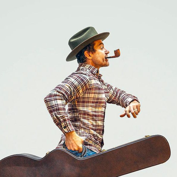 A man walking with a guitar while smoking a pipe
