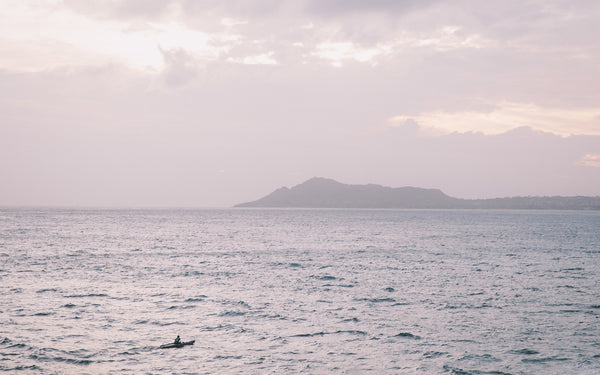 Wide shot of a sea kayaker, crossing in front of an island way in the background.
