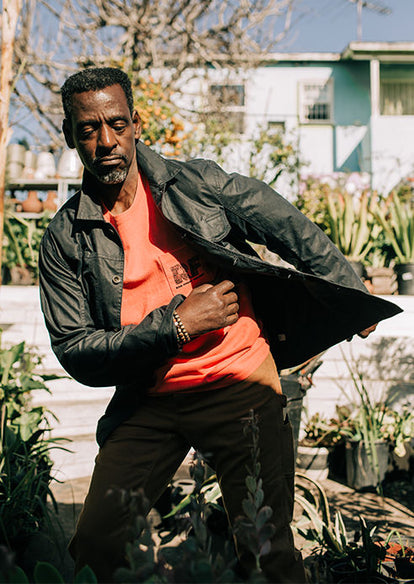 Ron dancing in his garden while wearing The Heavy Bag Tee in Hibiscus and The Carpenter Pant in Cedar Boss Duck.