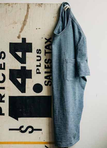 The Organic Cotton Tee in Dyed Indigo hanging on a vintage sign