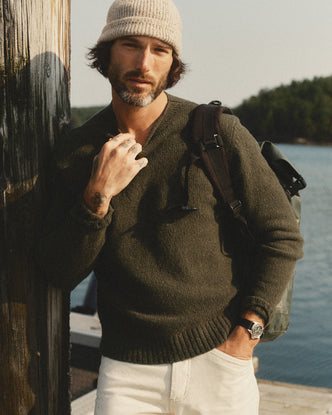 fit model leaning against a pole wearing The Seafarer Rollneck Sweater in Olive Donegal