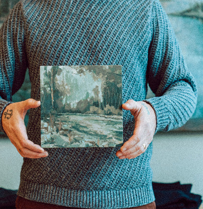 Zach Hixson holding up a landscape painting of the Oregon Coast.