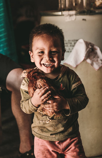 A child, smiling broadly, holding a chicken.