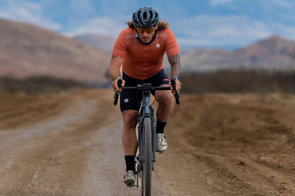 Yuri in an orange vest cycling by a mountain range