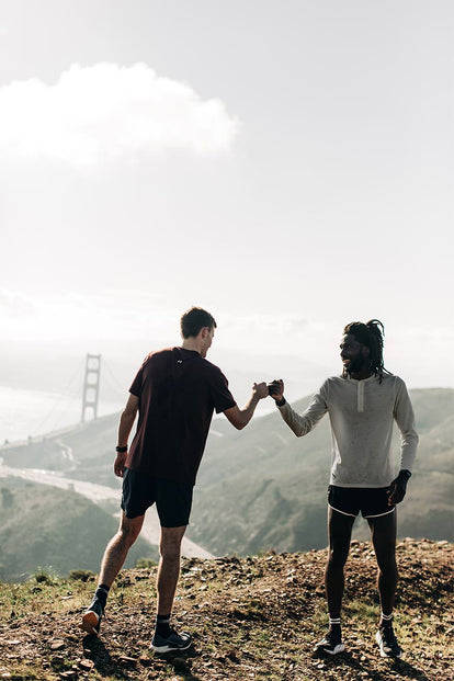 Two guys standing on a trail, fist-bumping, with The Golden Gate Bridge in the background.