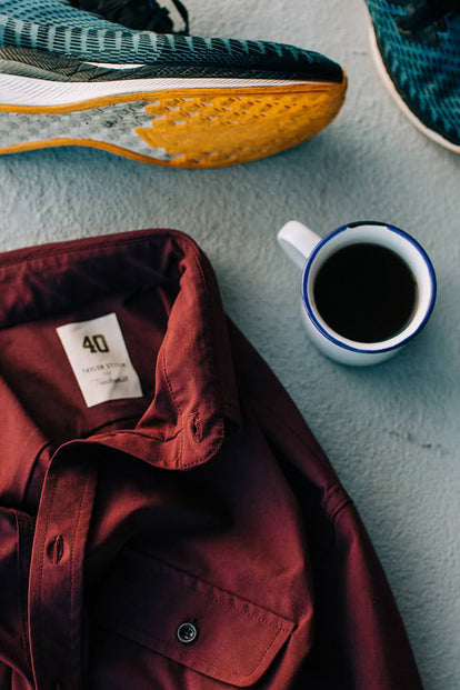 A flatlay shot featuring a red button-down shirt, sneakers, and a cup of black coffee.