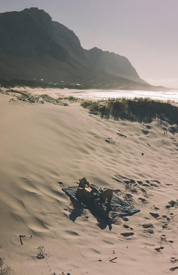 Relazing on a sand dune, reading a book.