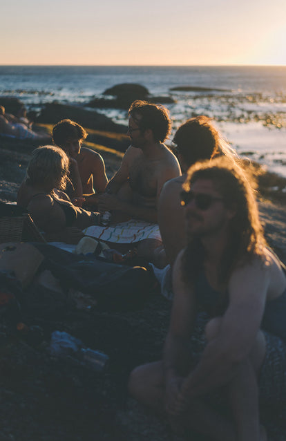 Various people socializing on a beach with sun coming in at a low angle.