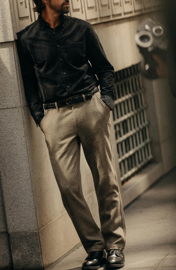 fit model leaning against the wall wearing The Carnegie Pant in Gravel Herringbone Wool