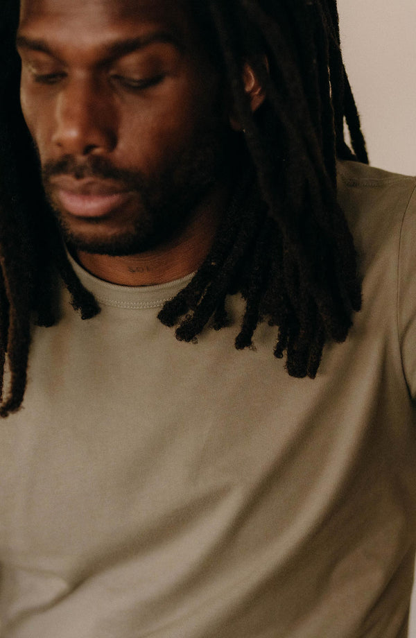 fit model leaning against a chair wearing The Organic Cotton Tee in Sage