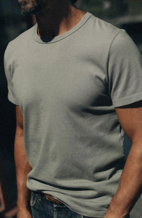 fit model leaning against a chair wearing The Organic Cotton Tee in Sage