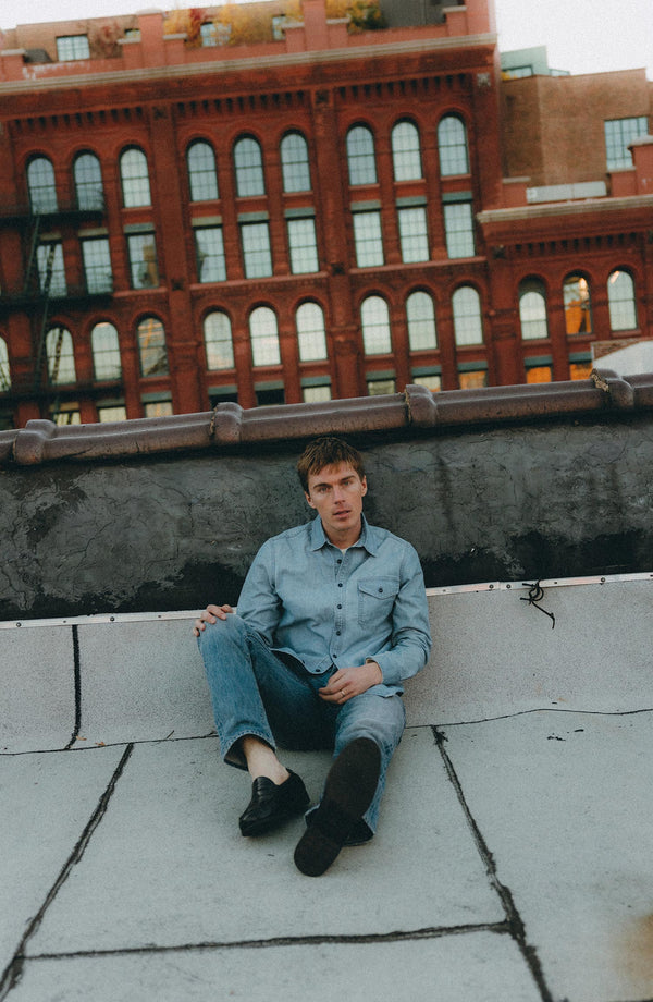 fit model sitting wearing The Cadet Shirt in Washed Indigo Oxford