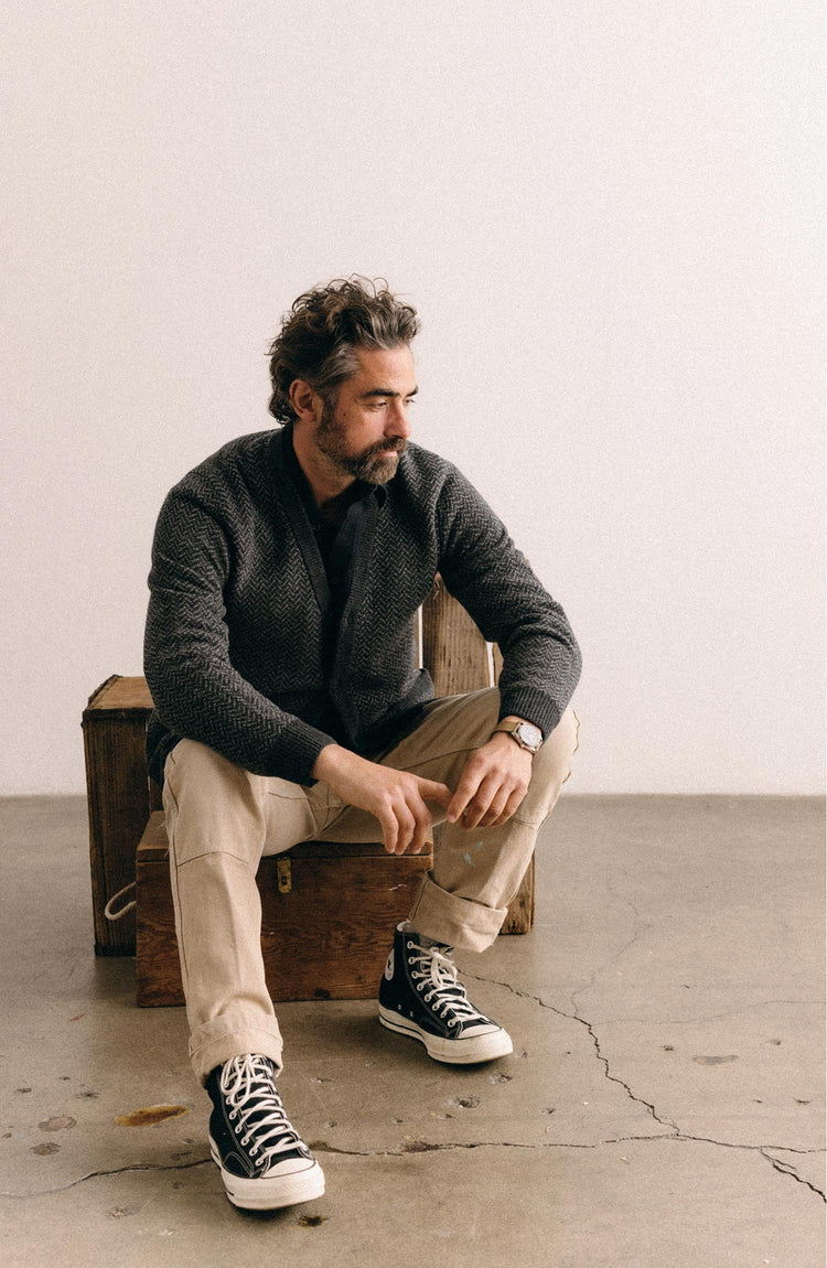 fit model sitting wearing The Eddy Cardigan in Heather Charcoal Herringbone