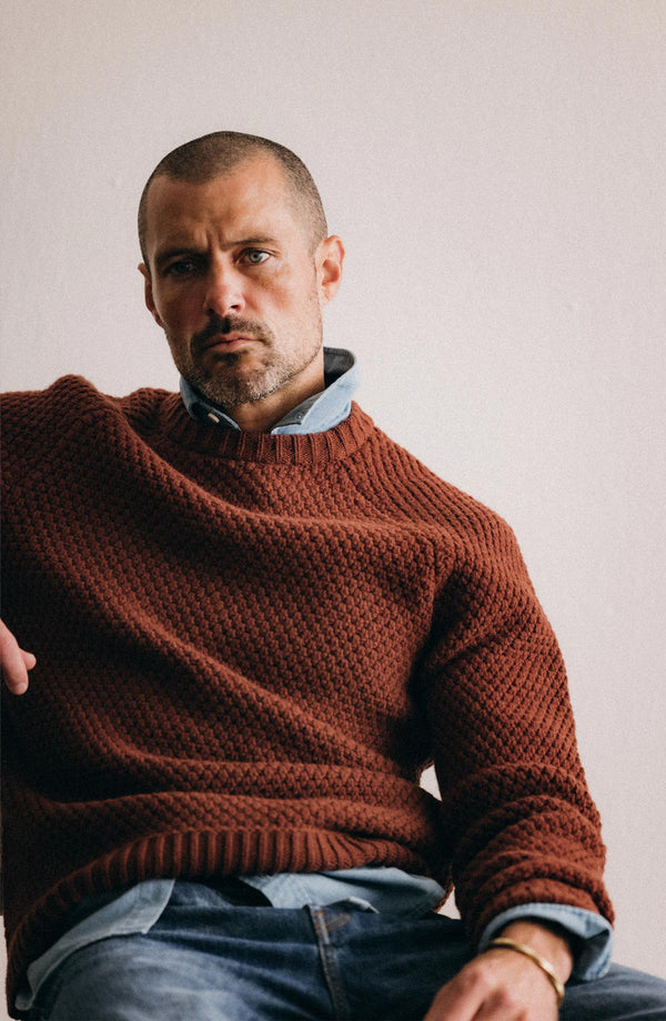 fit model sitting wearing The Fisherman Sweater in Heather Brick Merino