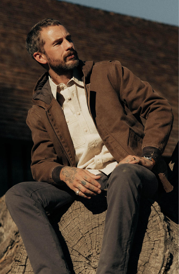 fit model sitting on a stump wearing The Workhorse Hoodie in Aged Penny Chipped Canvas
