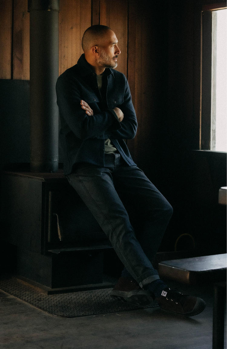 fit model leaning against a wood pile wearing The Camp Pant in Coal Chipped Canvas