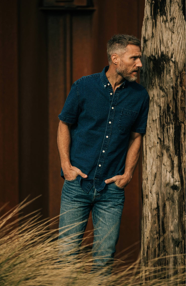 Model wearing The Short Sleeve Jack in Indigo Seersucker while leaning on a tree trunk”