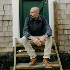 fit model sitting on wooden steps in The Utility Shirt in Rinsed Indigo Stripe