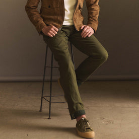fit model sitting on a stool wearing The Democratic Jean in Olive Nihon Menpu Selvage
