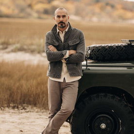 fit model leaning against a car wearing The Long Haul Jacket in Shale Cord