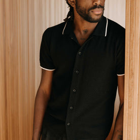 fit model leaning against the wall wearing The Button Down Polo in Coal Herringbone
