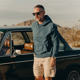 fit model posing next to a car wearing The Apres Hoodie in Washed Indigo Terry
