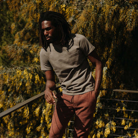 fit model leaning against a railing wearing The Heavy Bag Tee In Smoked Olive