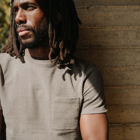 fit model leaning against the wall wearing The Heavy Bag Tee In Smoked Olive