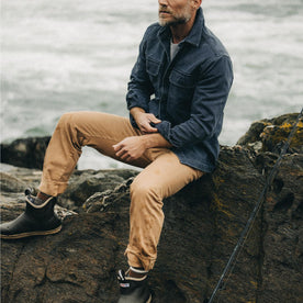 fit model sitting on a rock wearing The Democratic All Day Pant in Tobacco Selvage Denim
