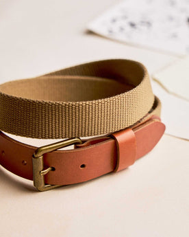 editorial image of The Webbed Belt in Whiskey rolled up on pieces of paper, Accessories by Taylor Stitch