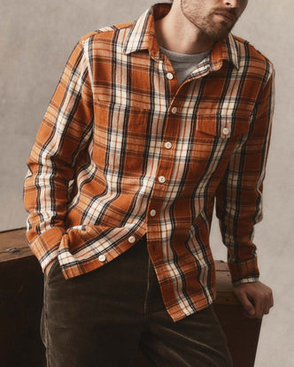 fit model holding a piece of wood wearing The Crater Shirt in Brick Plaid