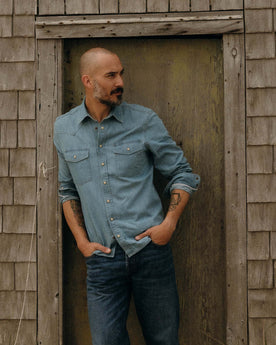 fit model leaning against the wall wearing The Glacier Shirt in Washed Indigo Denim, Wovens by Taylor Stitch