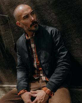 fit model sitting wearing The Insulated Bomber Jacket in Dark Navy Dry Wax, Outerwear by Taylor Stitch