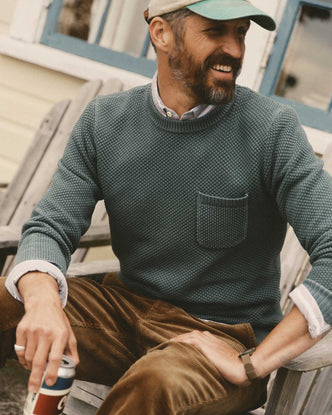 fit model sitting wearing The Crawford Crew Sweater in Faded Spruce