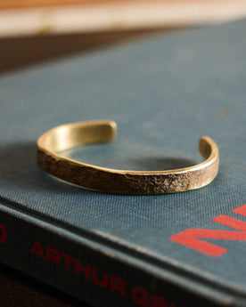 The Hammered Cuff in Brass on a book, Accessories by Taylor Stitch