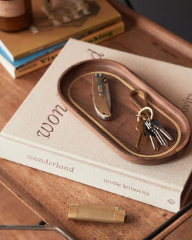 The Valet Tray in Walnut and Brass on a book, Accessories by Taylor Stitch