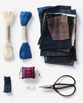 The thread, recycled denim patches, ashiko needles, pins and cushion and needle threader in the Sashiko Denim Repair Kit, Accessories by Taylor Stitch