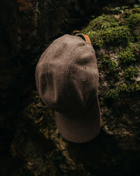 editorial image of The 5-Panel Cap in Heather Sable Wool Blend on a rock, Accessories by Taylor Stitch