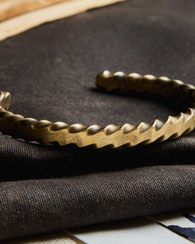 editorial image of The Twisted Cuff in Brass on a piece of fabric, Accessories by Taylor Stitch