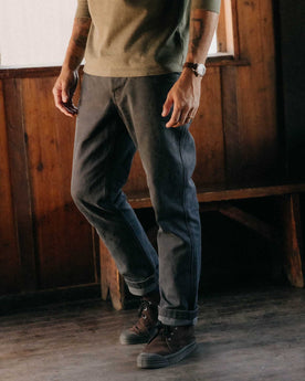 fit model leaning against a wood pile wearing The Camp Pant in Coal Chipped Canvas, Bottoms by Taylor Stitch