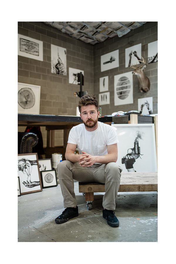 Jack Ludlam posing in his photography studio with prints surrounding him
