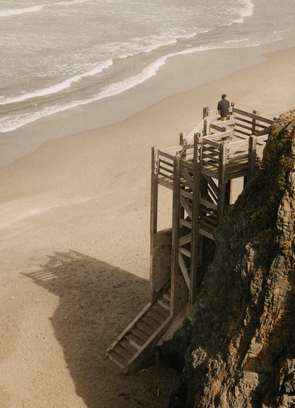 Model standing on a wooden staircase looking out at the ocean