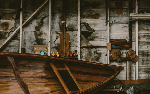 A well-used boat shed with tools and bows of a wooden row boat in the foreground.