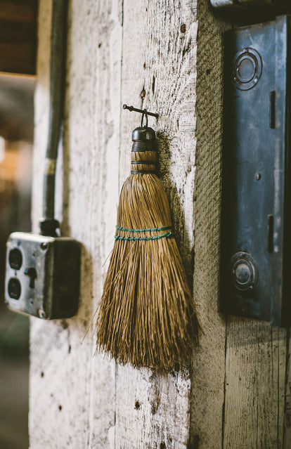 A broomhead hanging on a nail next to a lightswitch.