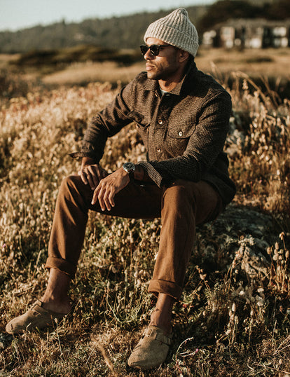 Our guy in a long haul jacket and workwear pants, sitting in a sunny field.