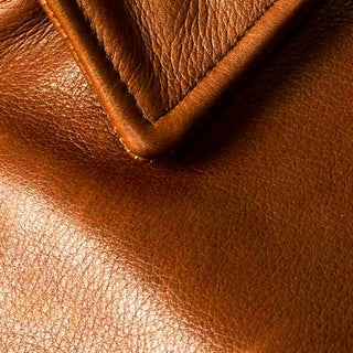 Closeup image of a glossy, light brown leather jacket - the corner of its collar is visible. 