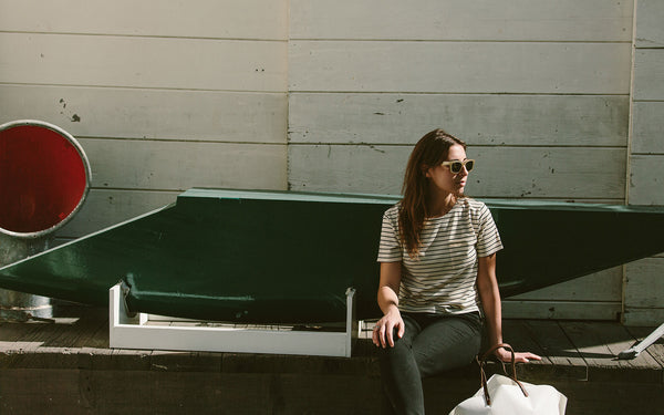 A woman sitting against a white wooden building.