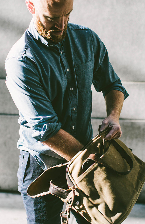 Our guy rummaging in his bag, wearing a rolled up denim shirt.